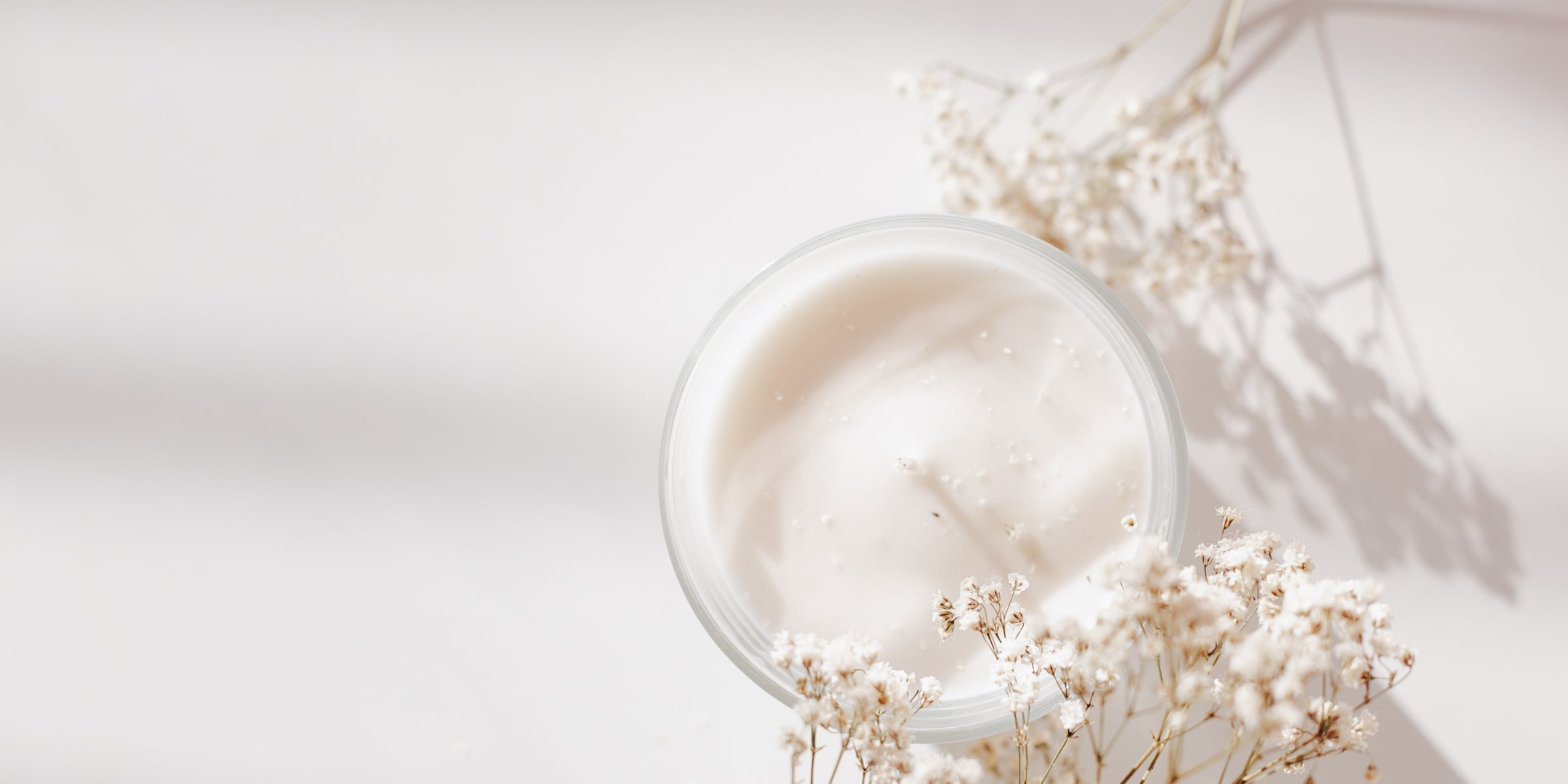 Bougie artisanale YuleSens en cire végétale, présentée dans un verre transparent, entourée de fleurs de gypsophile, ambiance douce et lumineuse.