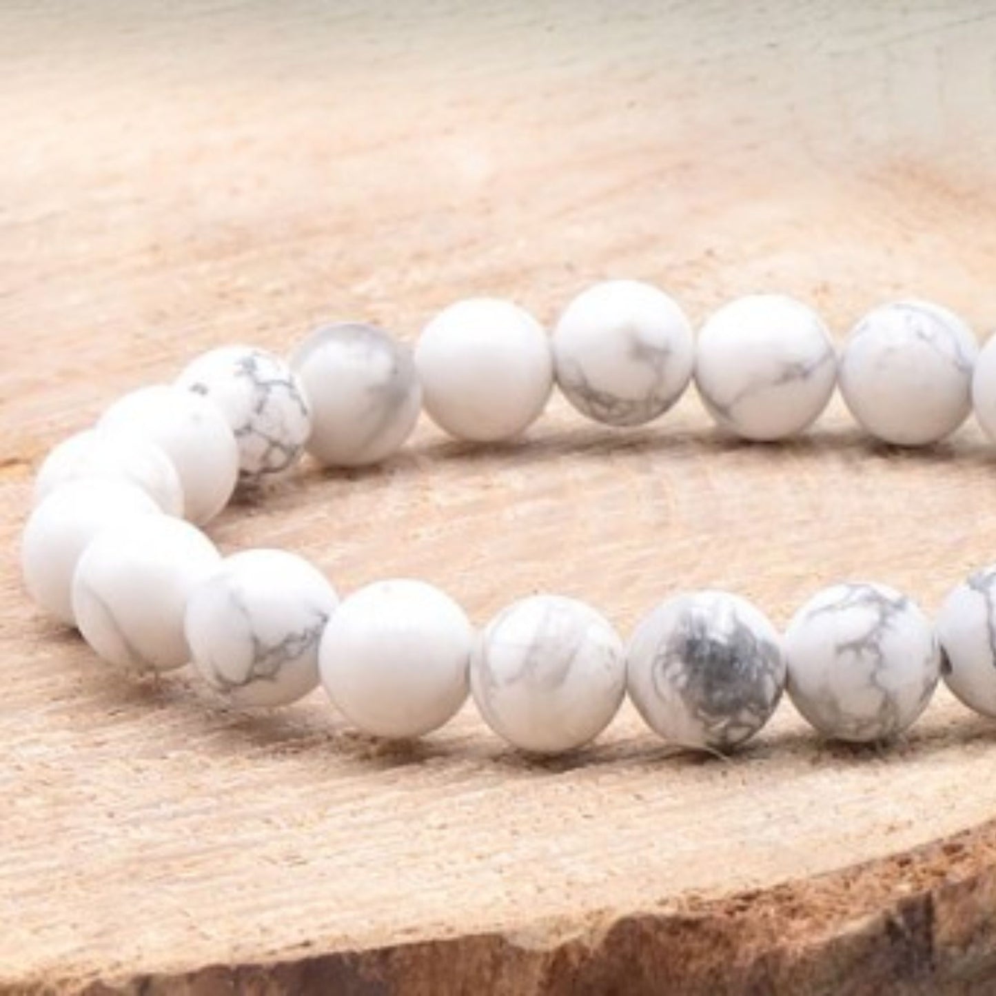 Bracelet en pierres naturelles de howlite blanche posé sur un rondin de bois clair, style épuré et naturel.