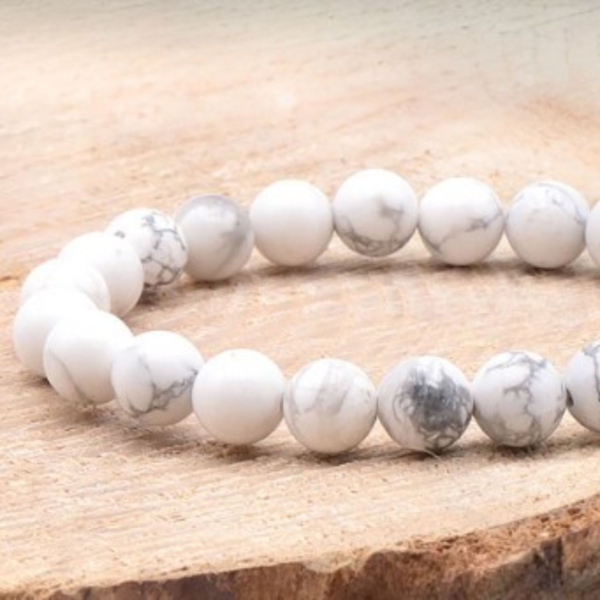 Bracelet en pierres naturelles de howlite blanche posé sur un rondin de bois clair, style épuré et naturel.